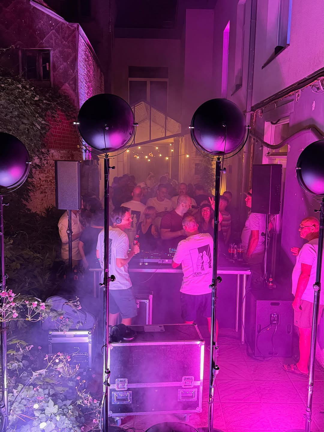 Volle binnenkoer bij nacht, de dj's achter de booth in roze licht.