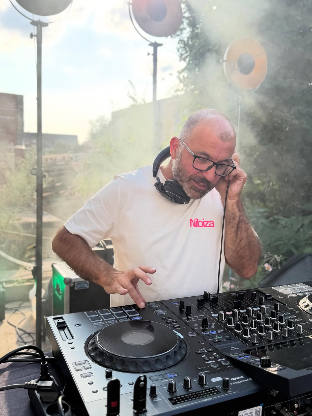 Een dj achter de decks terwijl de lage zon door de nevel breekt.