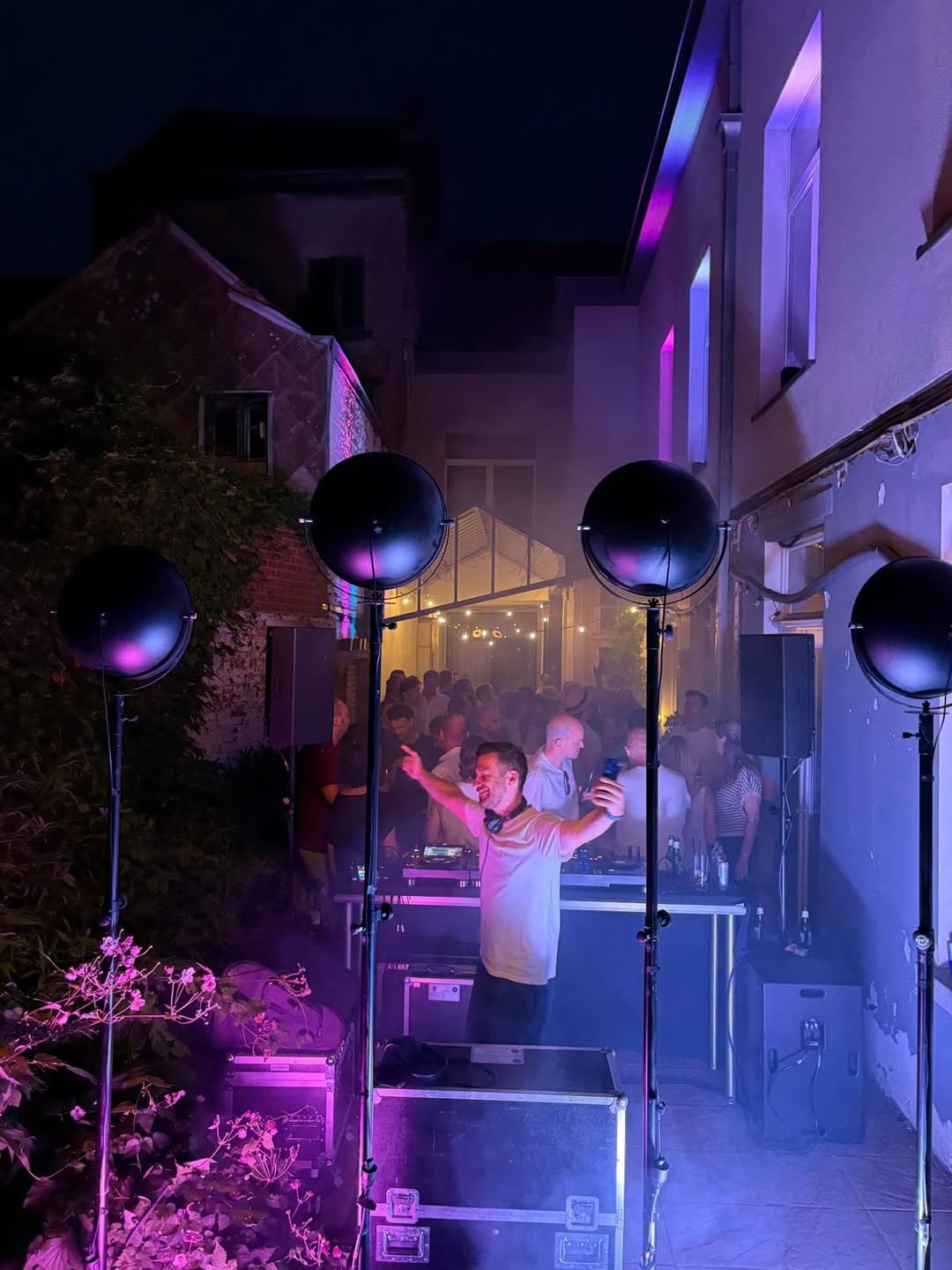 Een dj met de armen wijd achter de booth, paars licht en volle koer.