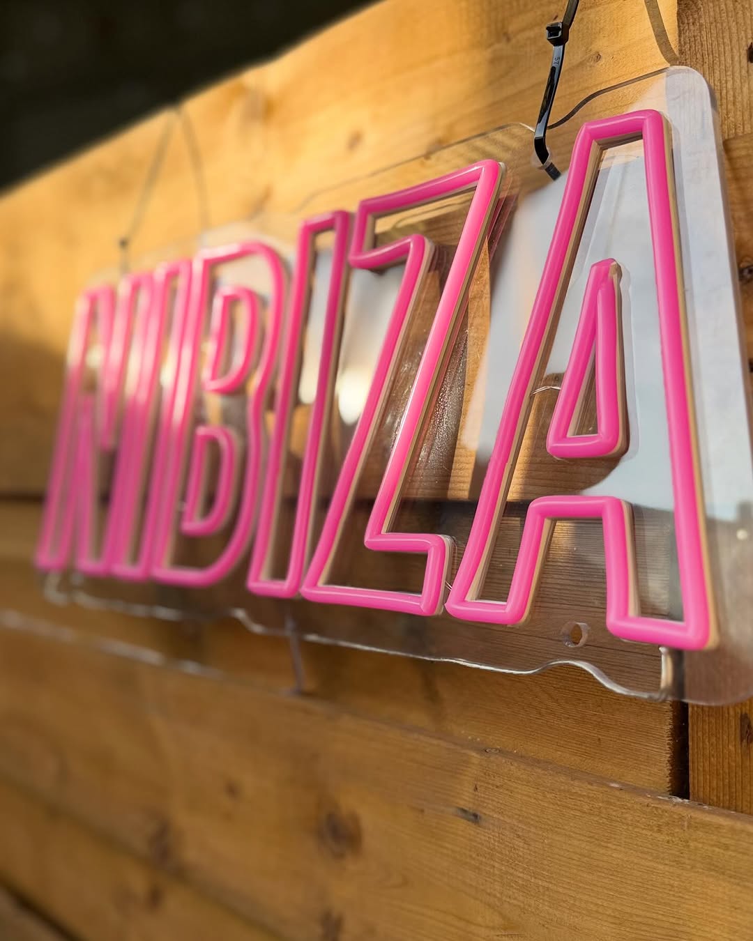 Het roze NIBIZA-neonbord aan een houten wand.